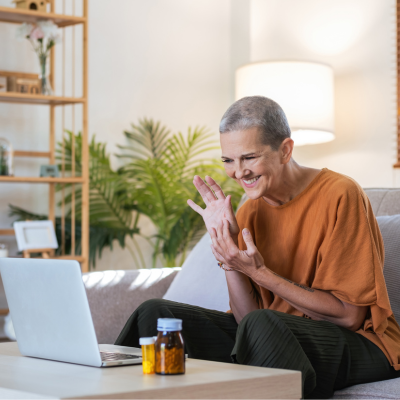 Senior-aged woman sitting on her couch and engaging with health professional on her laptop, representing telehealth and behavioral health integration