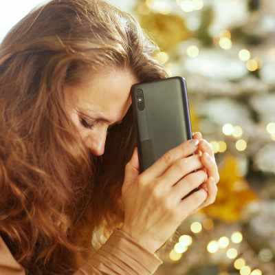 Coping with loneliness during the holidays: how to help patients navigate emotional challenges 8 Woman holding phone against her head while appearing depressed with a christmas tree in the background, representing coping with loneliness during the holidays